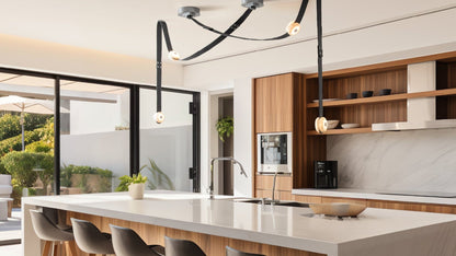 Modern kitchen interior with pendant LED lights over the countertop, surrounded by wooden cabinetry and white marble surfaces, with a view of a kitchen island and stools in the foreground.